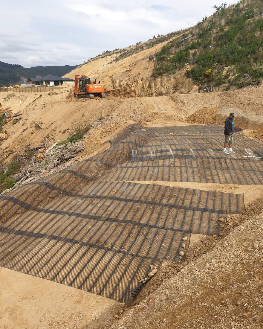 Layers of geogrid laid on a reinforced earth slope, with an excavator working at the top