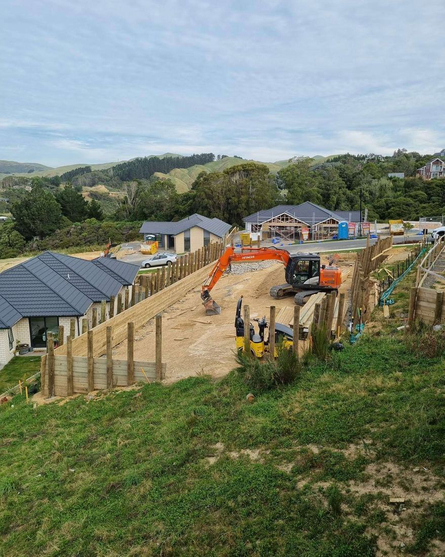 Hillside subdivision under construction, with a timber pole wall along the cut and new houses behind