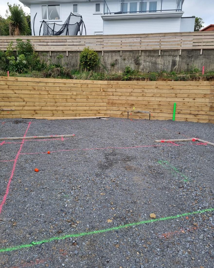 Levelled metal building platform marked out in spray paint below a new timber retaining wall