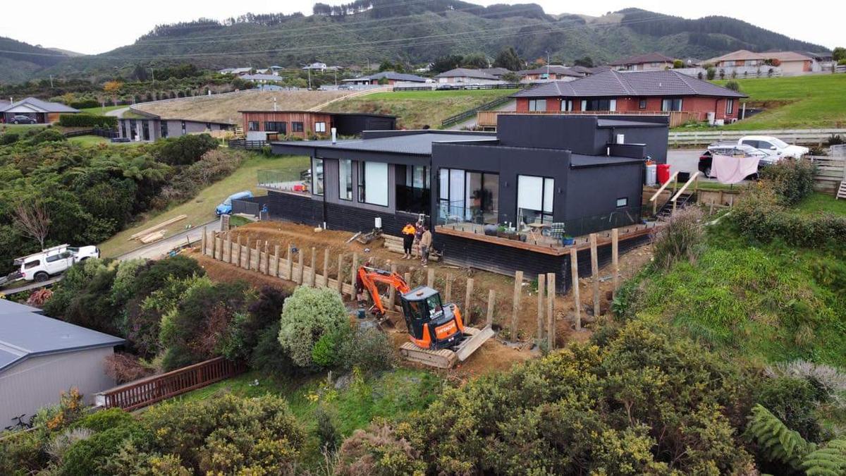 Elevated view of a timber pole retaining wall going in on the slope in front of a modern dark house
