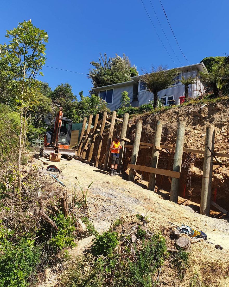 Crew building a timber pole retaining wall up a steep bush bank below a house