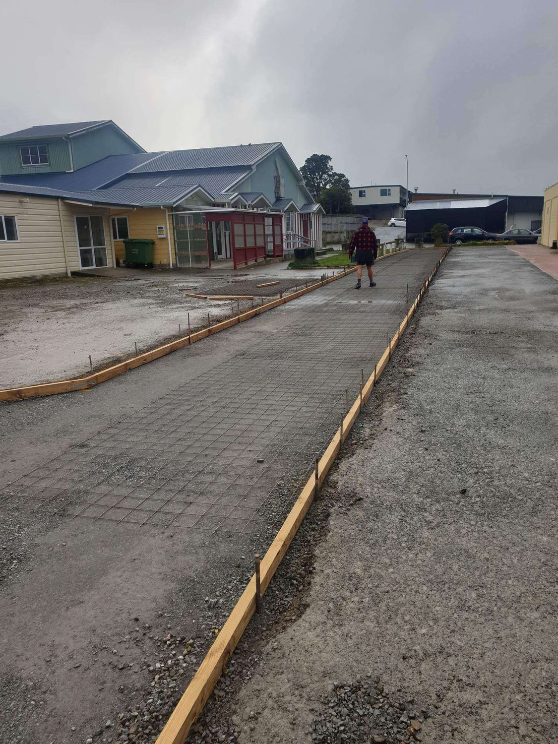 Reinforcing mesh inside timber boxing for a long concrete accessway, with a worker standing on site