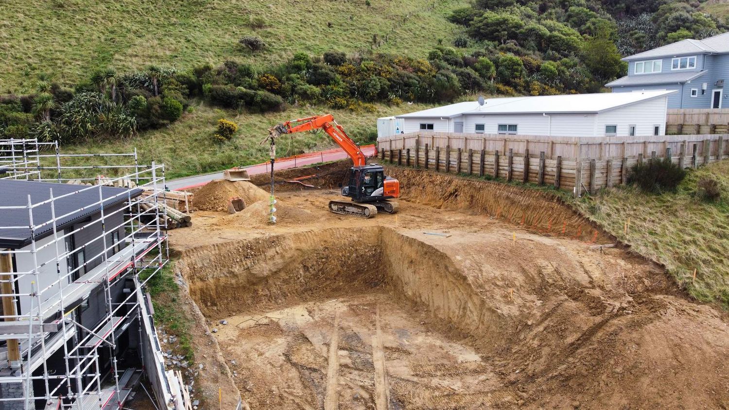 Aerial view of an excavator digging a foundation hole beside a building under scaffolding