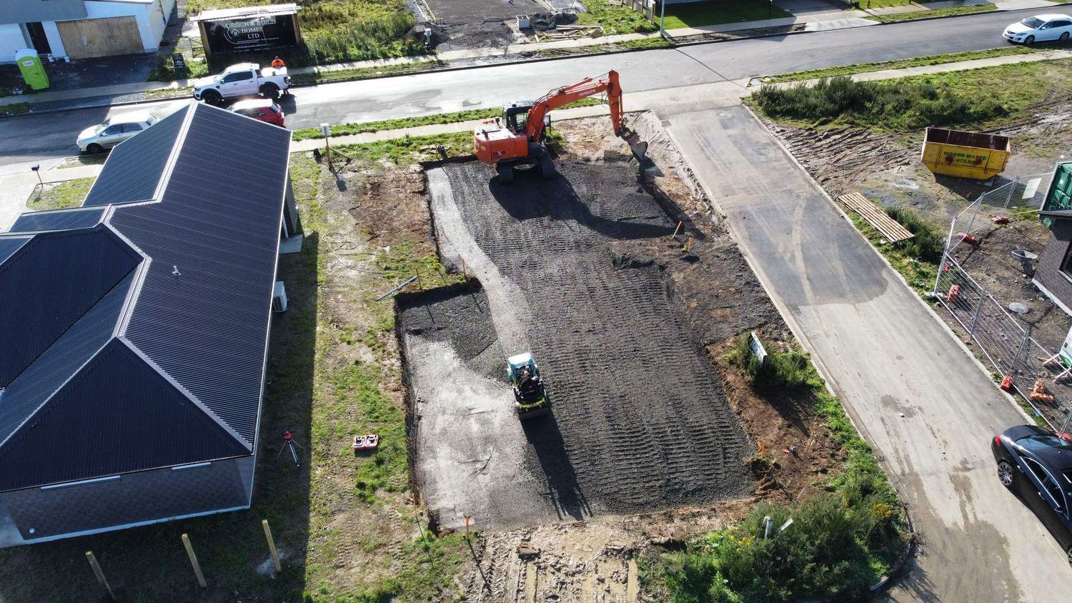 Drone view of a driveway being formed beside a new house, with an excavator and roller at work
