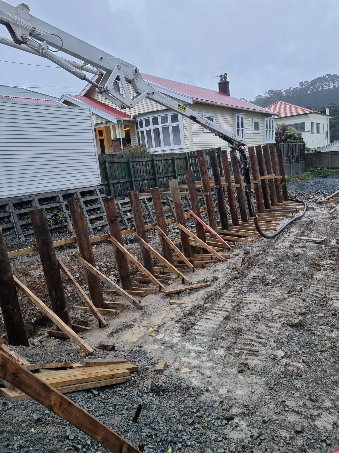 Concrete pump boom pouring into timber piles for a street-front retaining wall