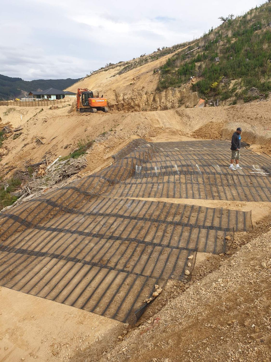 Geogrid rolled out across a reinforced earth slope while a worker checks the levels