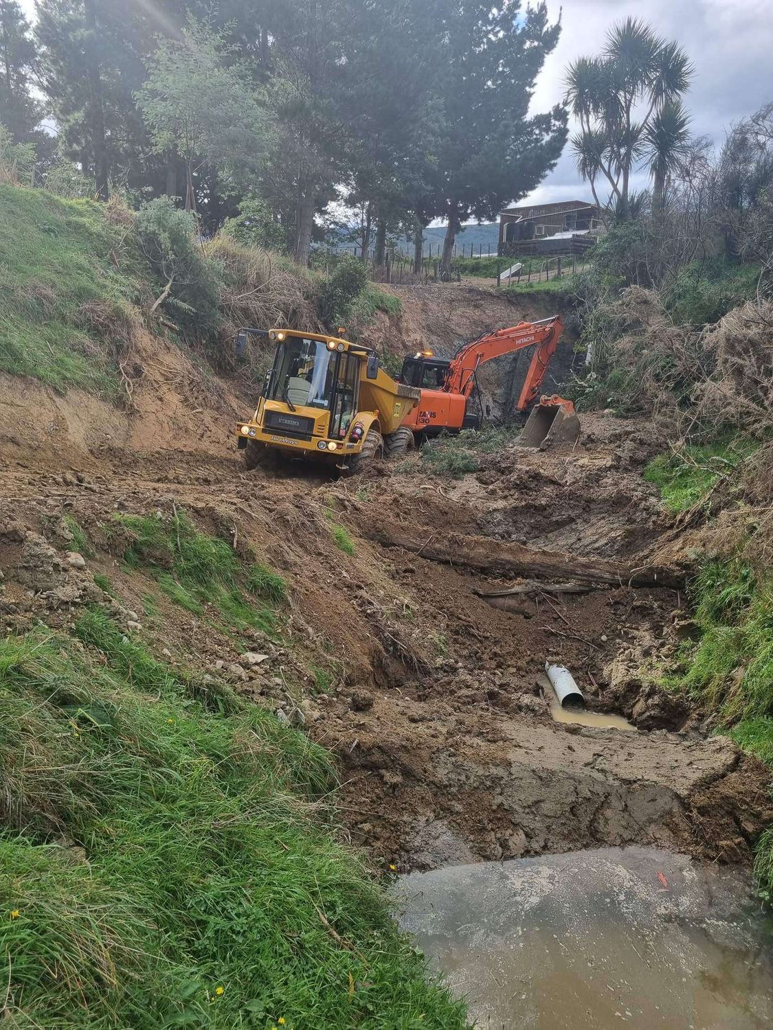 Wheel loader and excavator working in a stream gully beside a culvert outlet
