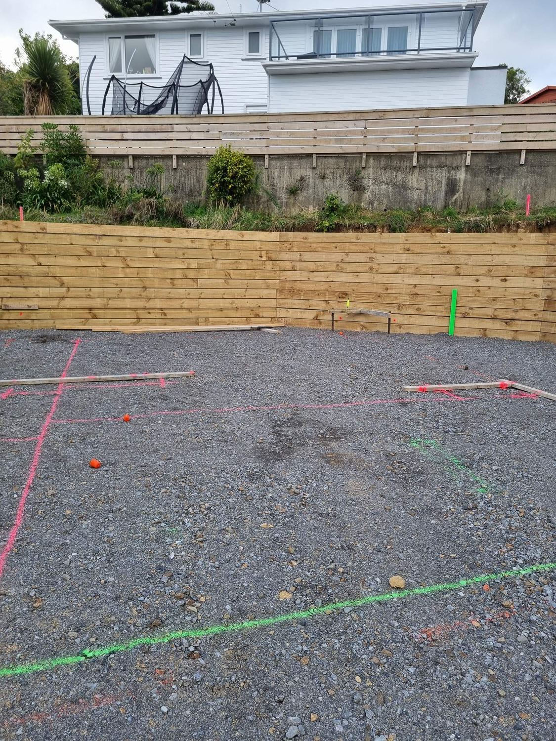 Metal building platform marked out in spray paint below a new timber retaining wall