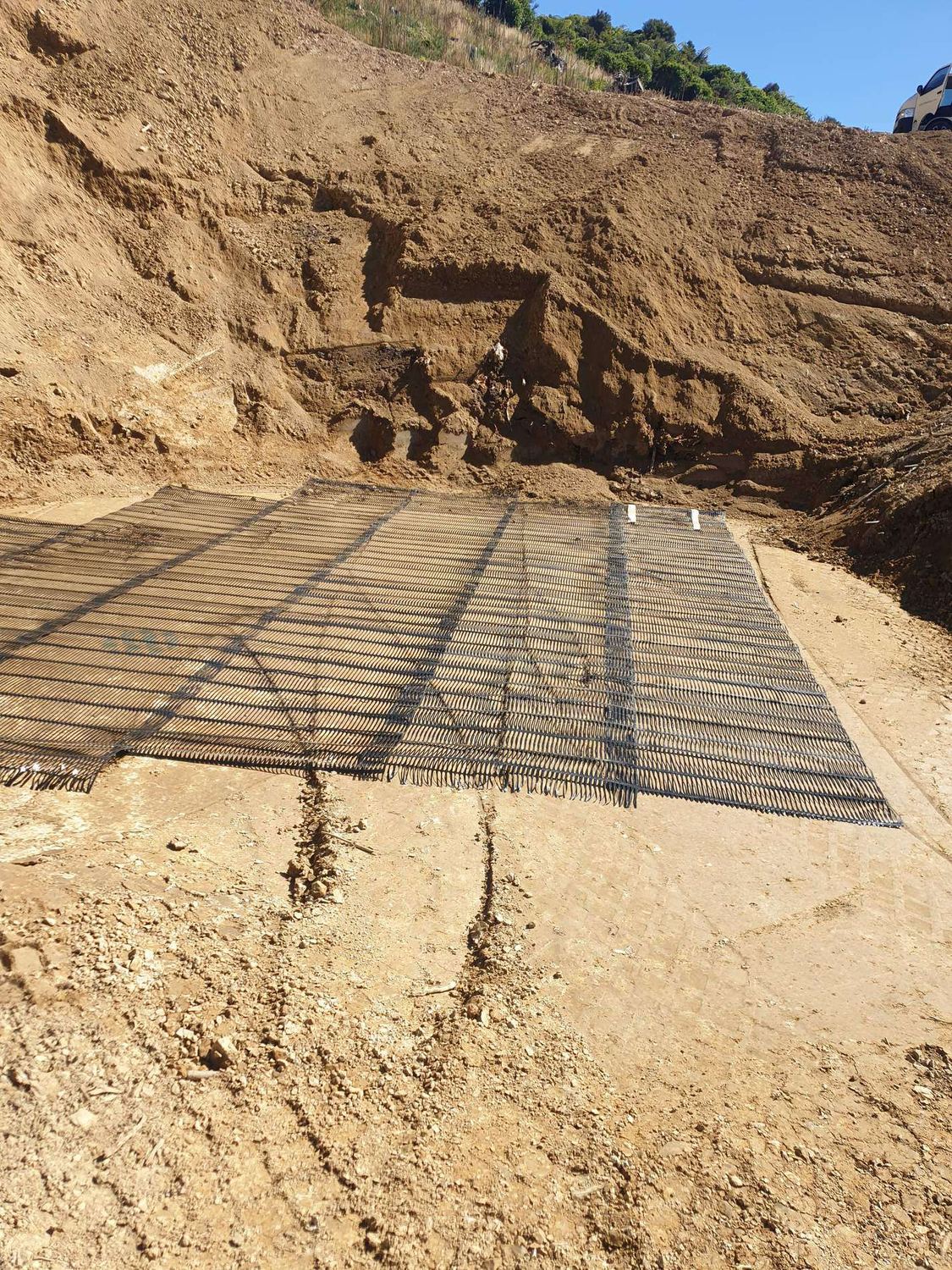 Steel reinforcing mesh laid on a levelled pad below a tall excavated bank
