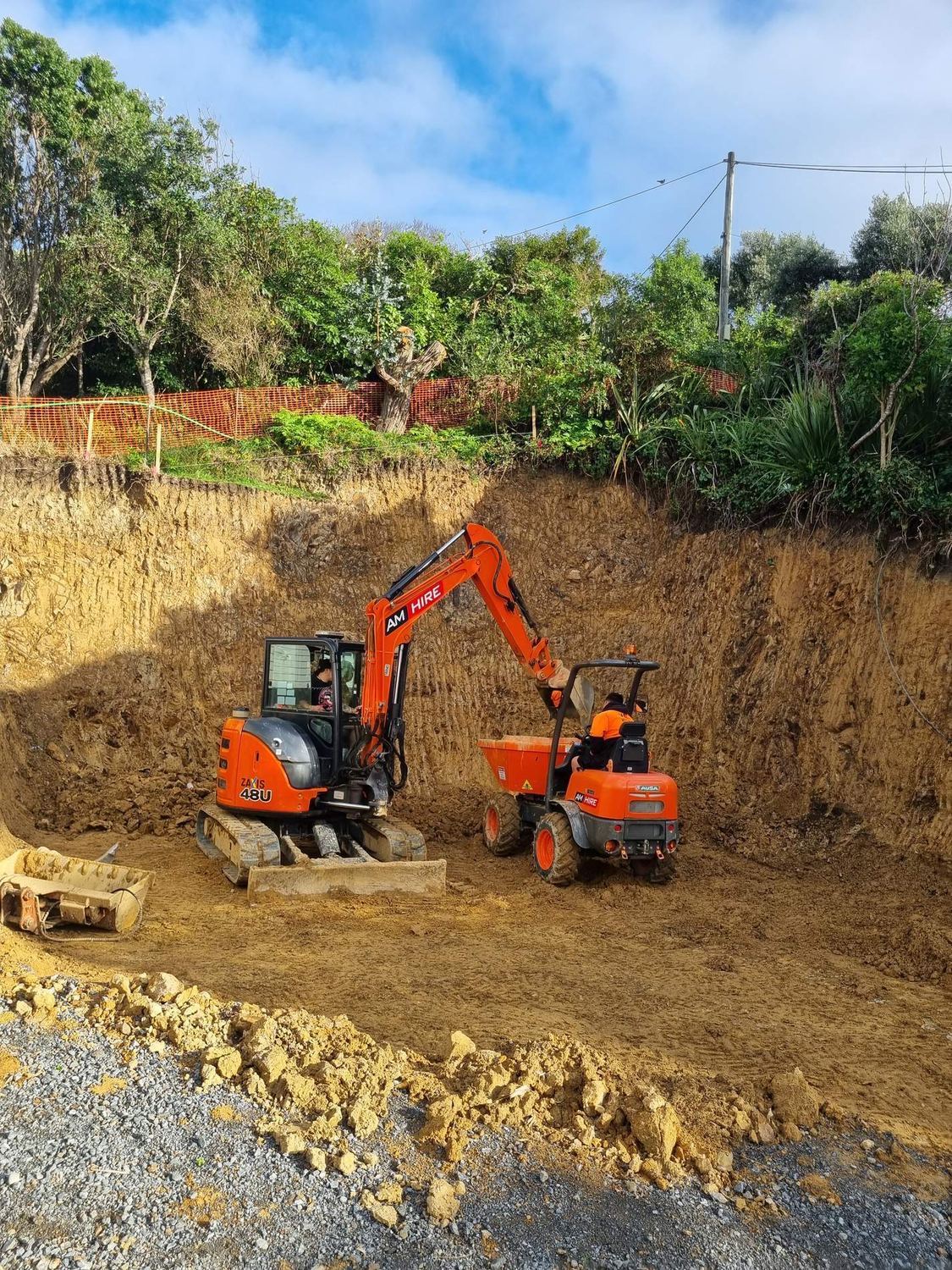 Mini excavator and tracked dumper levelling a cut platform below a bush bank