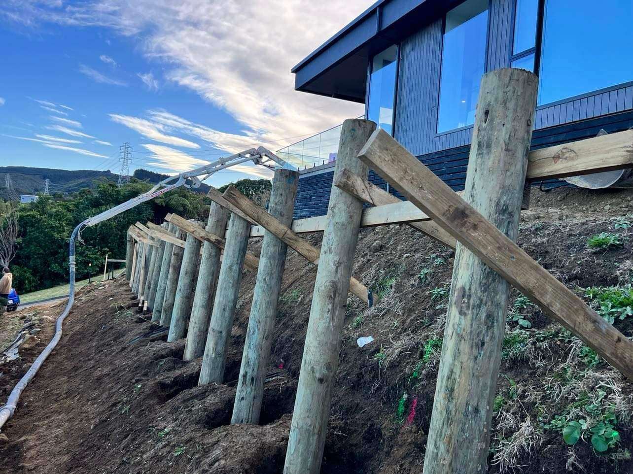Timber pole wall with raking rails under a modern house on a steep slope