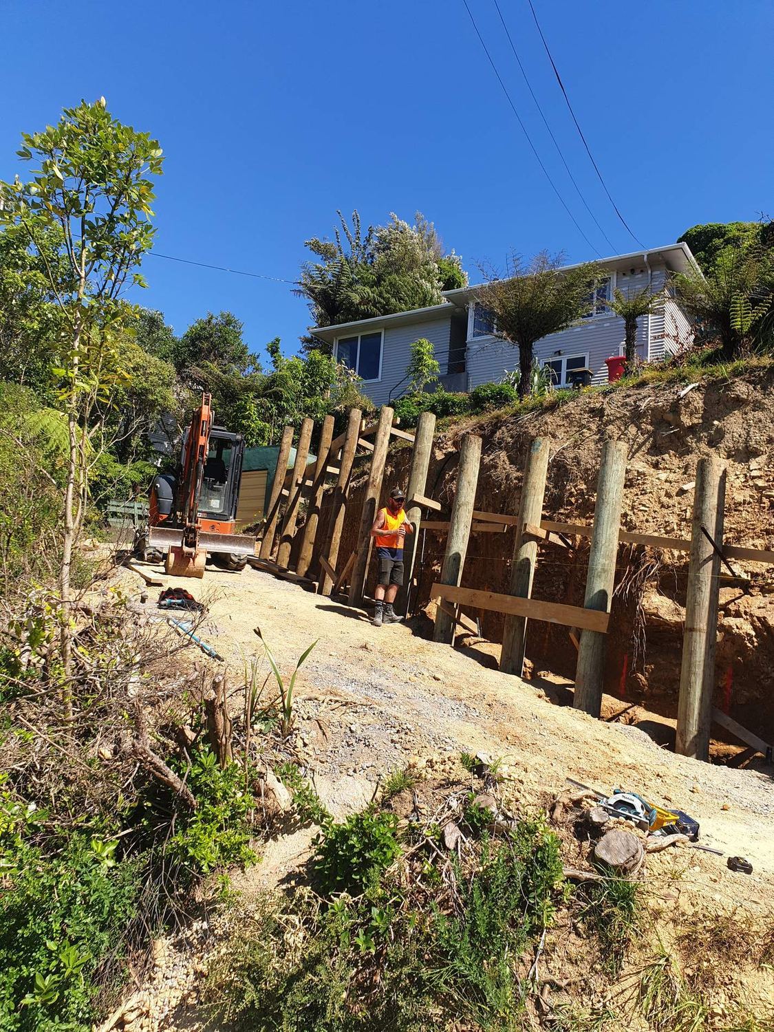 Crew building a timber pole retaining wall up a steep bank below a house
