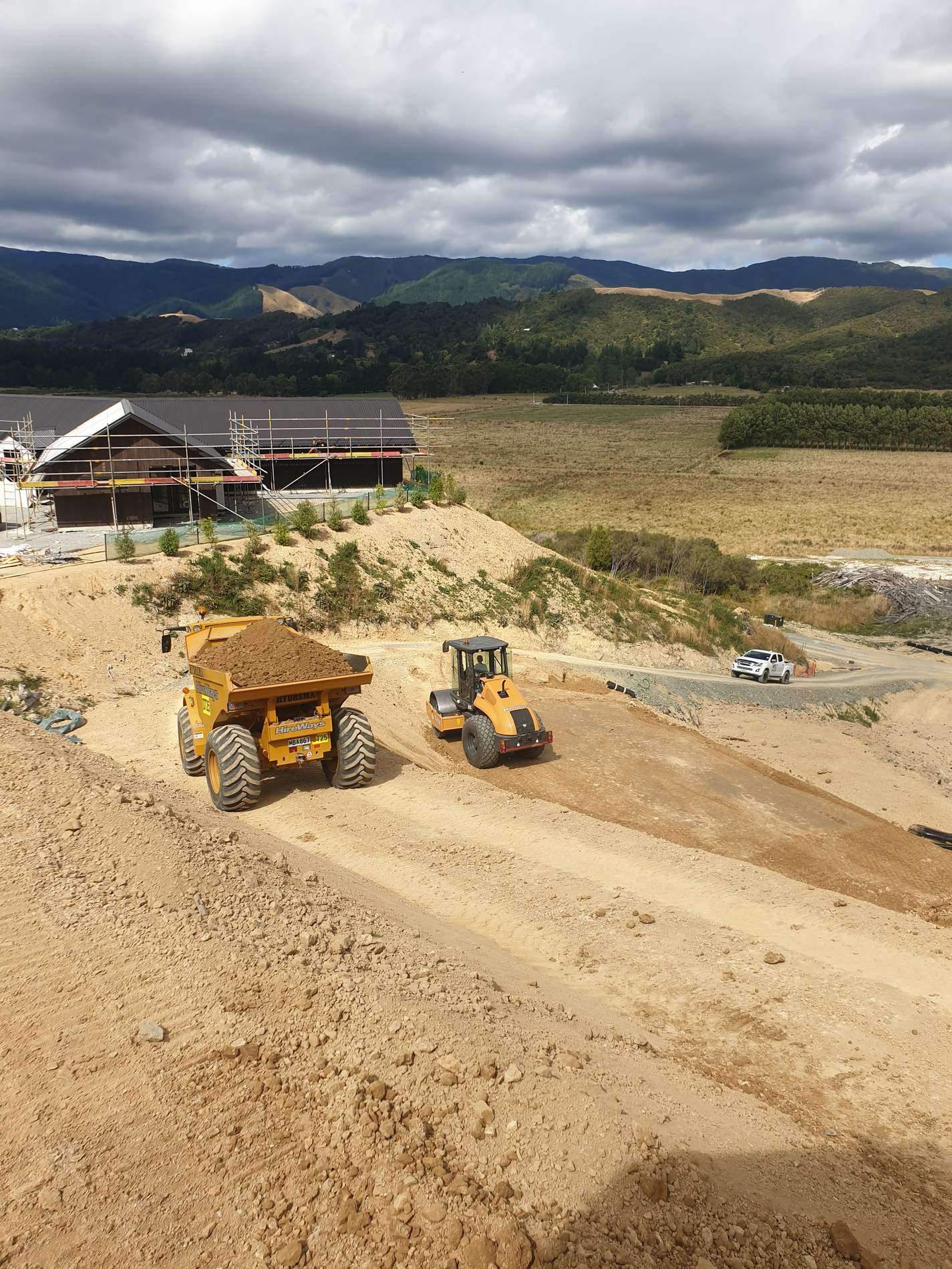 Articulated dump truck and wheel loader working a large earthworks cut beside a house under construction