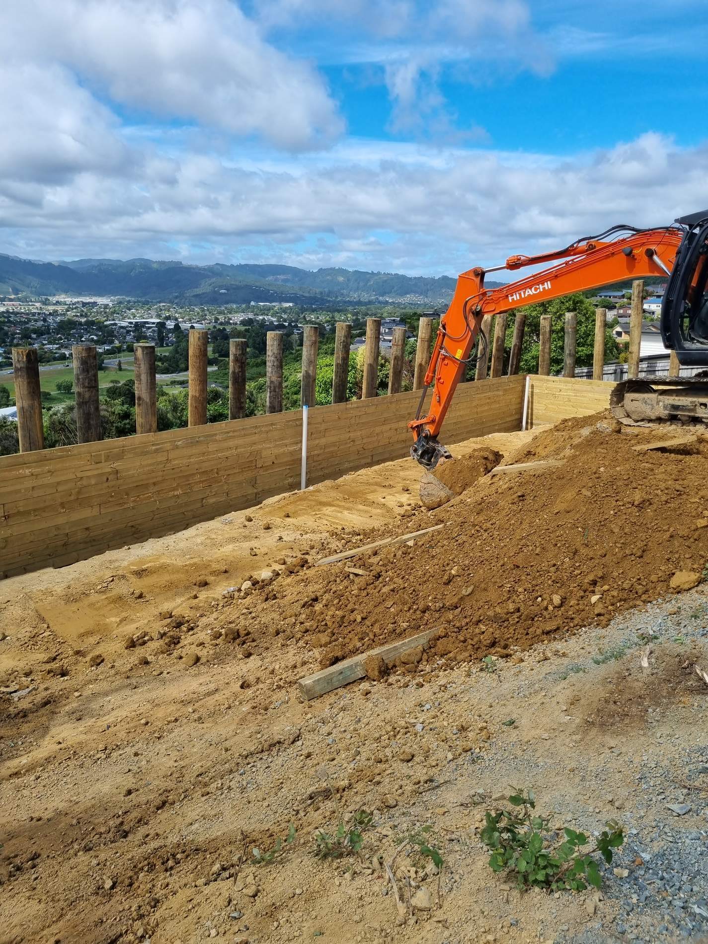Excavator spreading fill behind a new timber retaining wall above a valley