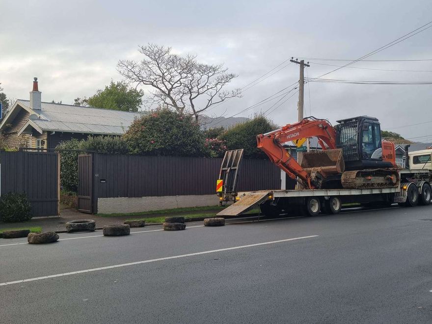 Excavator loaded on a truck and transporter trailer parked on a suburban street