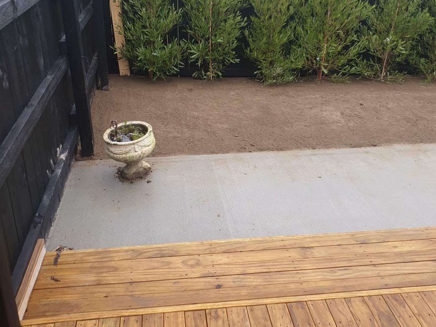 Finished backyard with a new timber deck, concrete patio and levelled garden beside a black fence