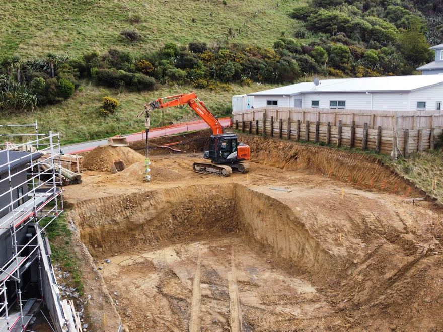 Aerial view of an excavator digging a foundation beside a building under scaffolding