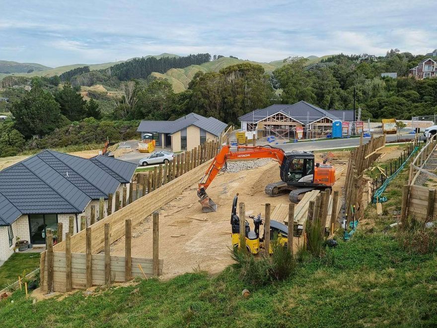 Excavator and roller forming a building platform behind a timber retaining wall in a hillside subdivision